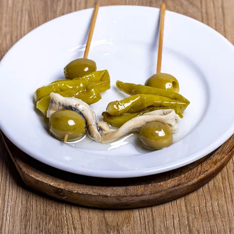 Gildas de anchoa con aceitunas y piparras en un plato blanco, sobre madera.
