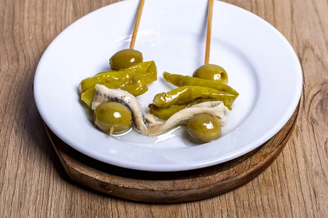 Gildas de anchoa con aceitunas y piparras en un plato blanco, sobre madera.