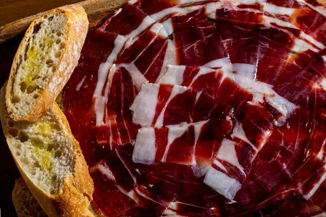 Jamón ibérico cortado a cuchillo con pan con aceite, en una tabla de madera.